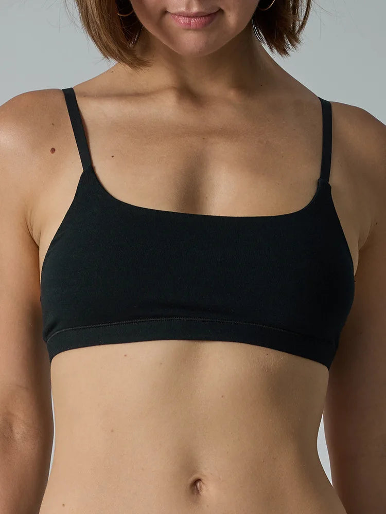 A close-up of a woman wearing a black square-neck bralette against a solid gray background.