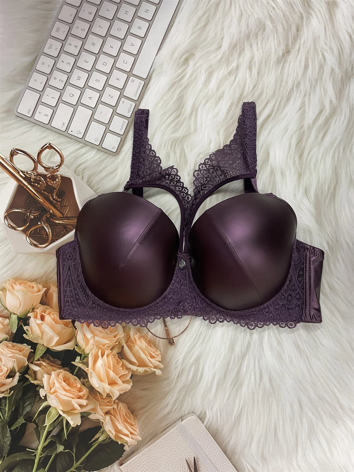 Purple bra with lace details on a white surface with flowers and a keyboard.
