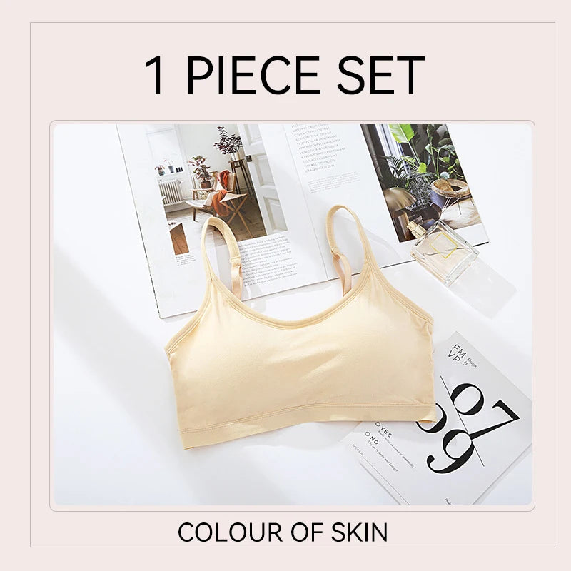A beige wireless bralette set displayed on a white surface with open magazines and a perfume bottle. Text at the top reads '1 PIECE SET' and text at the bottom reads 'COLOUR OF SKIN'.