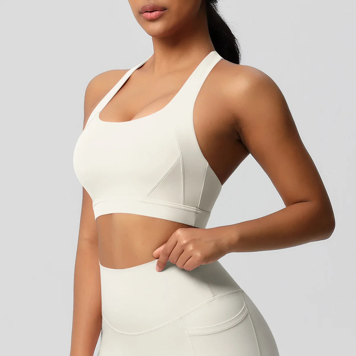 Woman wearing a white sports bra and leggings on a light gray background