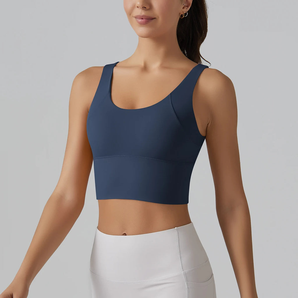 Woman wearing a navy blue sports bra and white leggings on a gray background