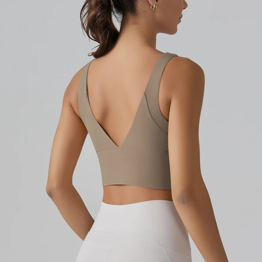 Woman wearing a beige sports bra and white leggings on a gray background
