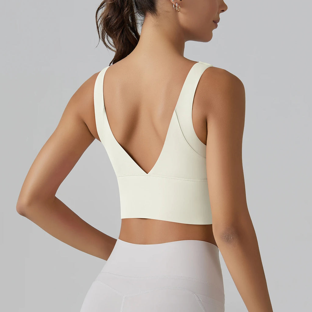 Woman wearing a beige sports bra and white leggings on a gray background