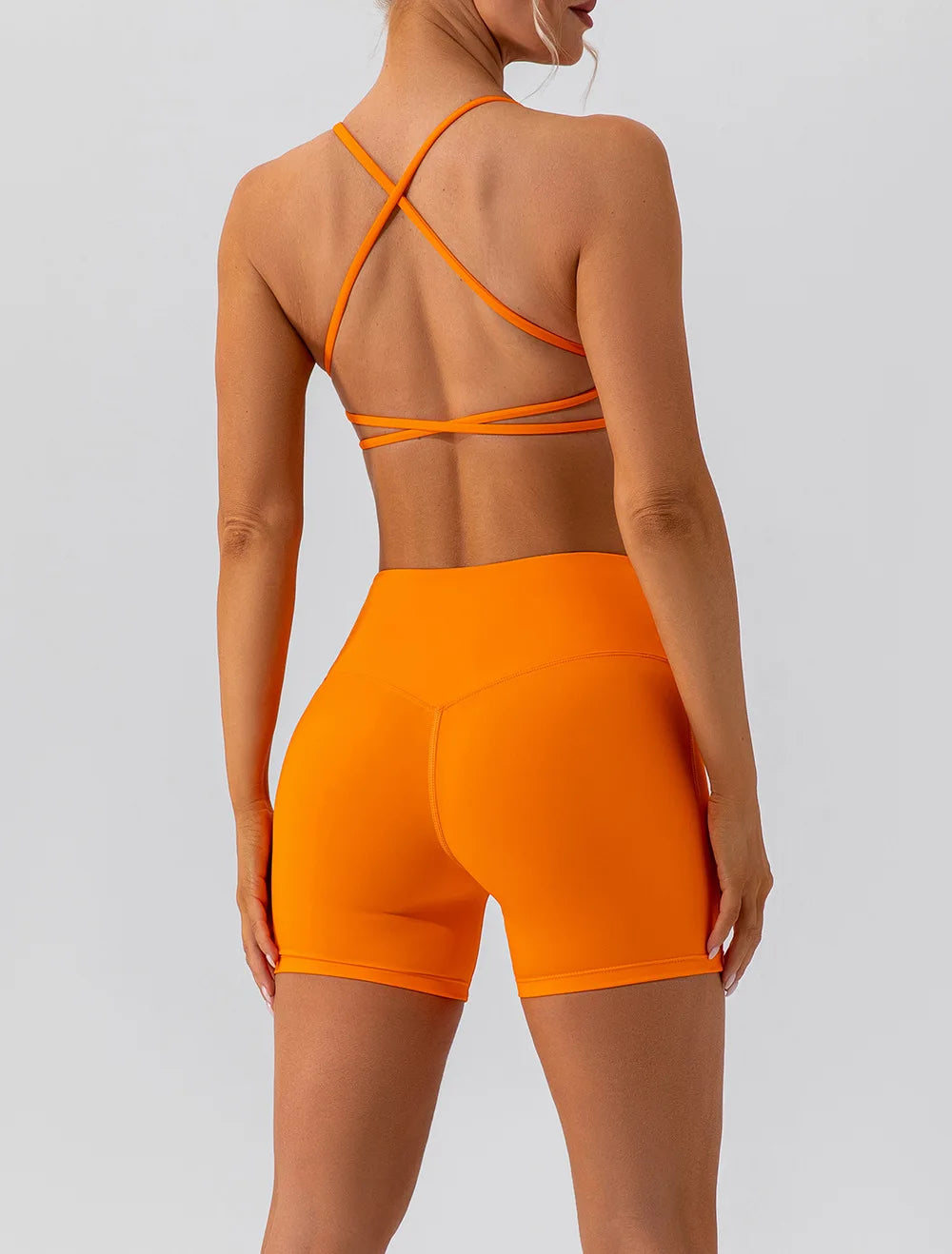 Person wearing an orange sports bra and shorts set on a light gray background
