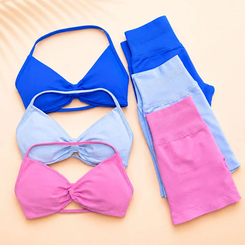 Three colorways of matching activewear sets are arranged on a warm beige background: a royal blue bikini top with matching blue leggings, a light blue bikini top with light blue leggings, and a pink bikini top with pink leggings.