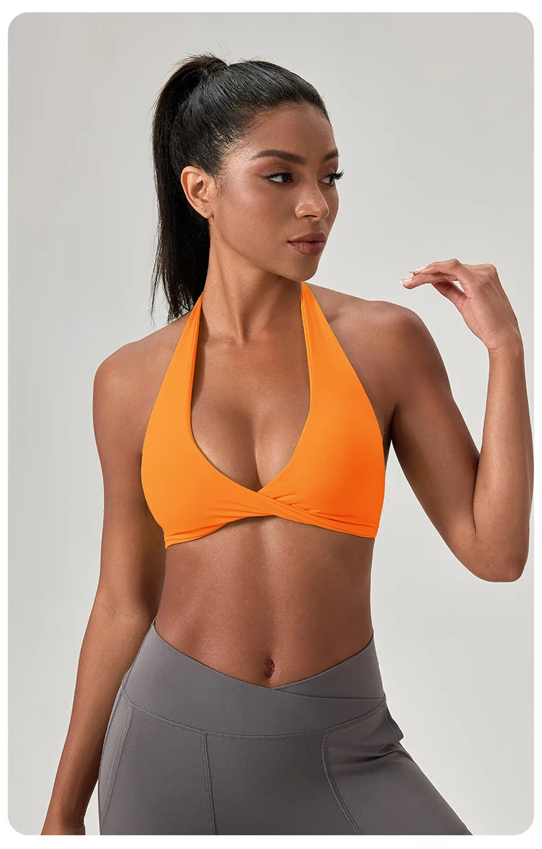 Woman wearing an orange sports bra and gray leggings on a light gray background