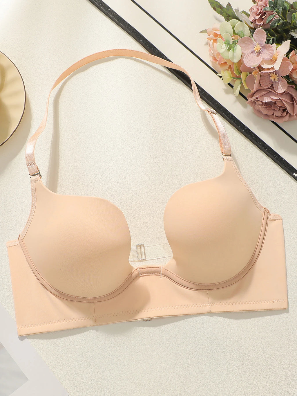 Beige bra on a white surface with decorative flowers in the background
