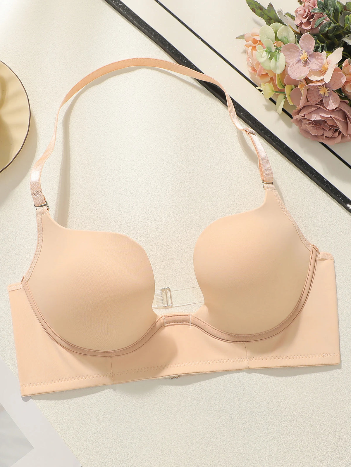 Beige bra on a white surface with decorative flowers in the background