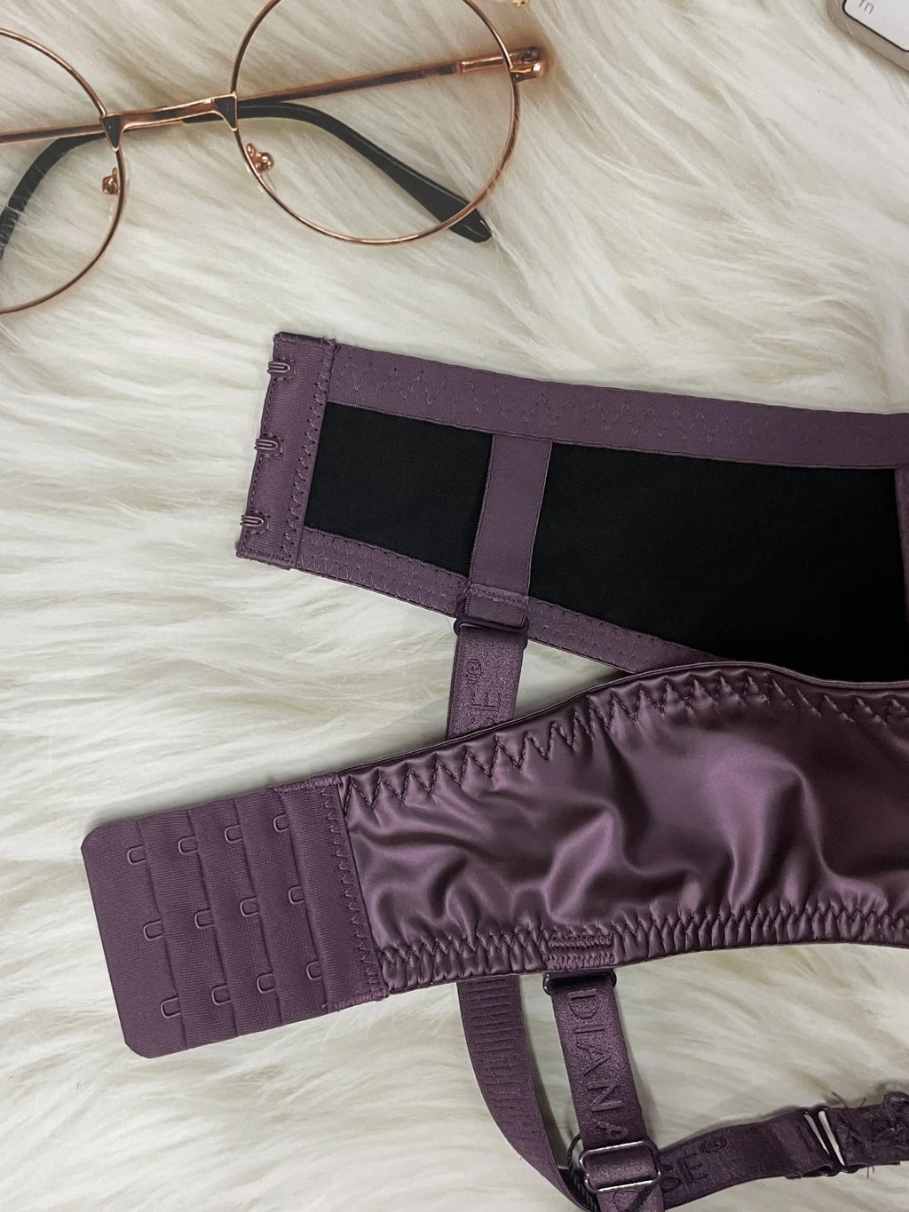 Purple satin eye mask on a white fluffy surface with glasses in the background