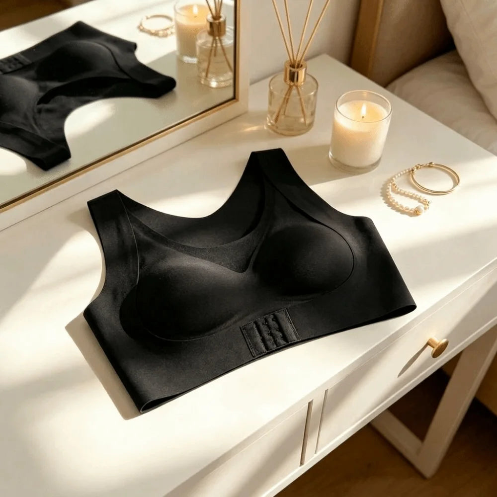 A black wireless bralette laid flat on a white dresser next to a mirror, candle, reed diffuser, and jewelry, with warm sunlight casting shadows.