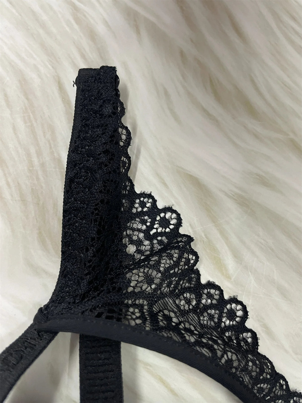 Black lace bra strap detail with floral lace trim, photographed on a soft white faux-fur background.