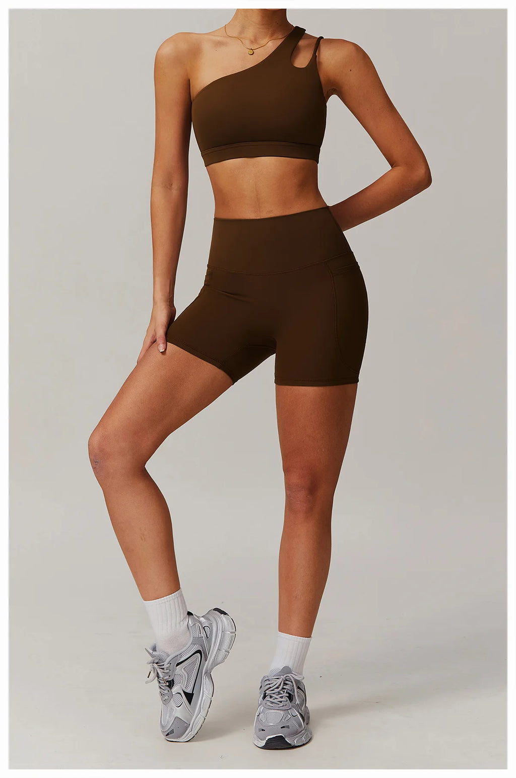 Person wearing a brown sports bra and shorts set with gray sneakers on a light gray background