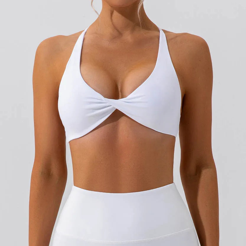 A woman wearing a white halter-style bikini top with a twisted front detail, paired with a matching white high-waisted bottom, shown against a plain light gray studio background.