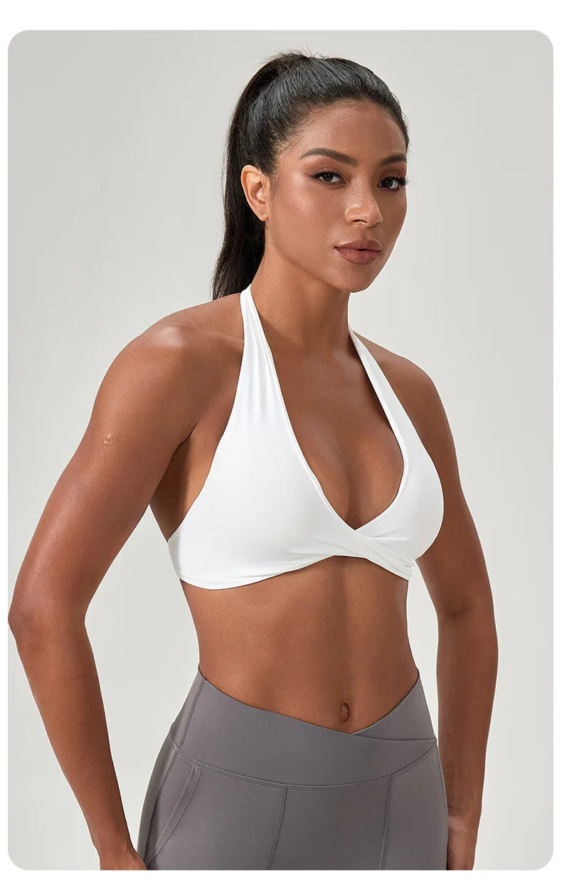 Woman wearing a white sports bra and gray leggings on a plain background