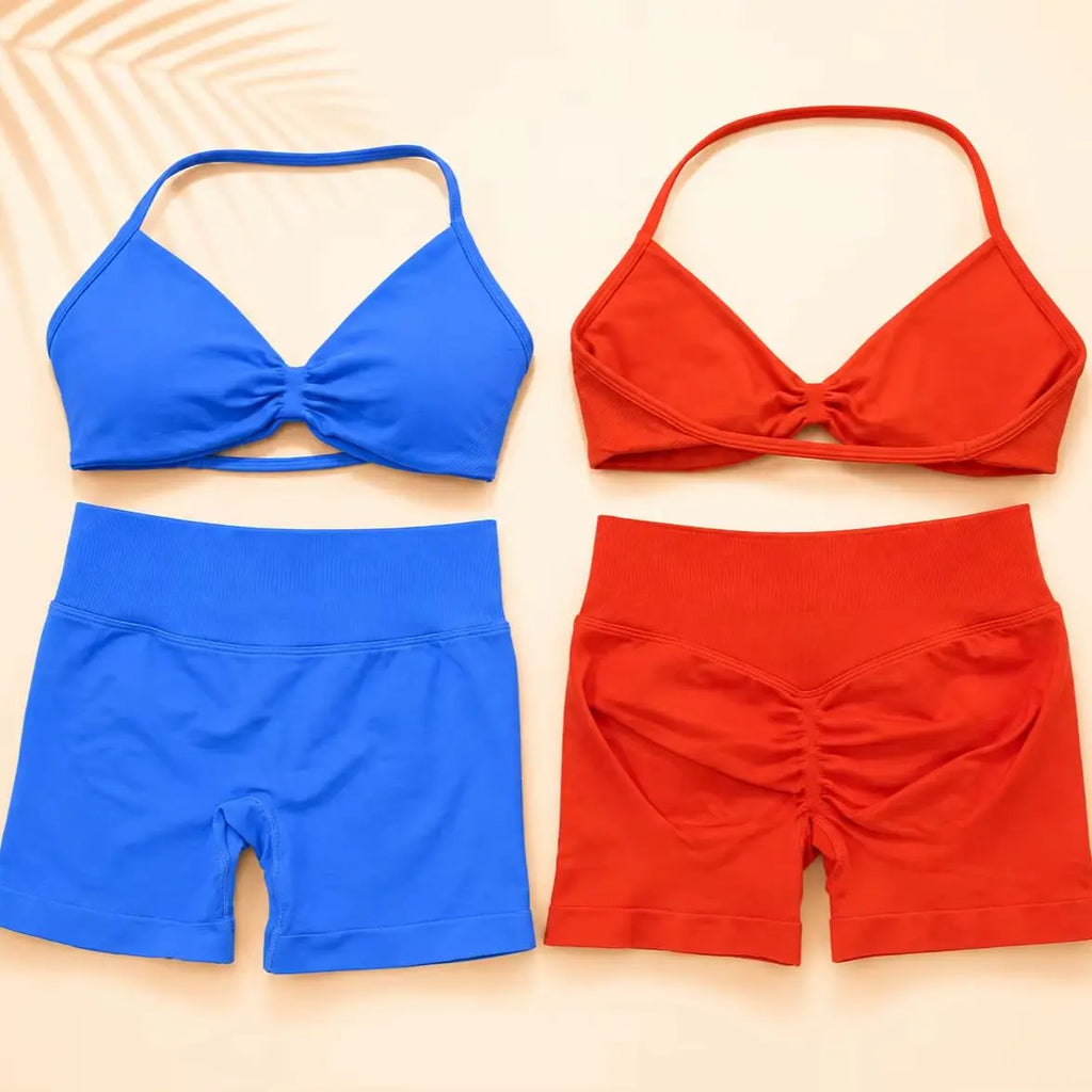 Two women's two-piece swimsuit sets laid flat on a light beige background. The top-left set is bright blue with a halter-style bikini top and high-waisted shorts.