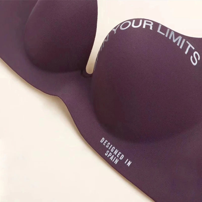 A close-up of a dark purple molded silicone bra pad with white printed text reading 'EXCEED YOUR LIMITS' and 'DESIGNED IN SPAIN' on a light beige background.
