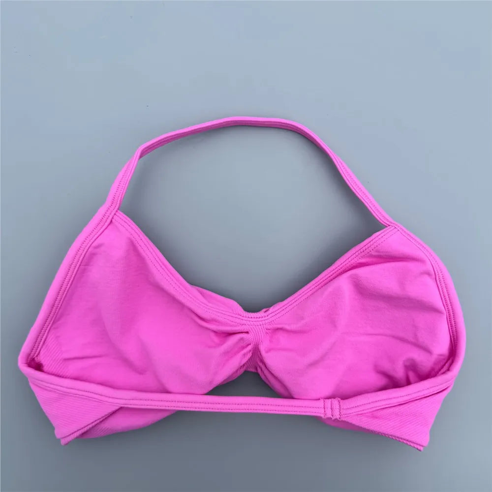 A bright pink bikini top or bralette with a halter-style strap and gathered center, laid flat on a smooth gray background.