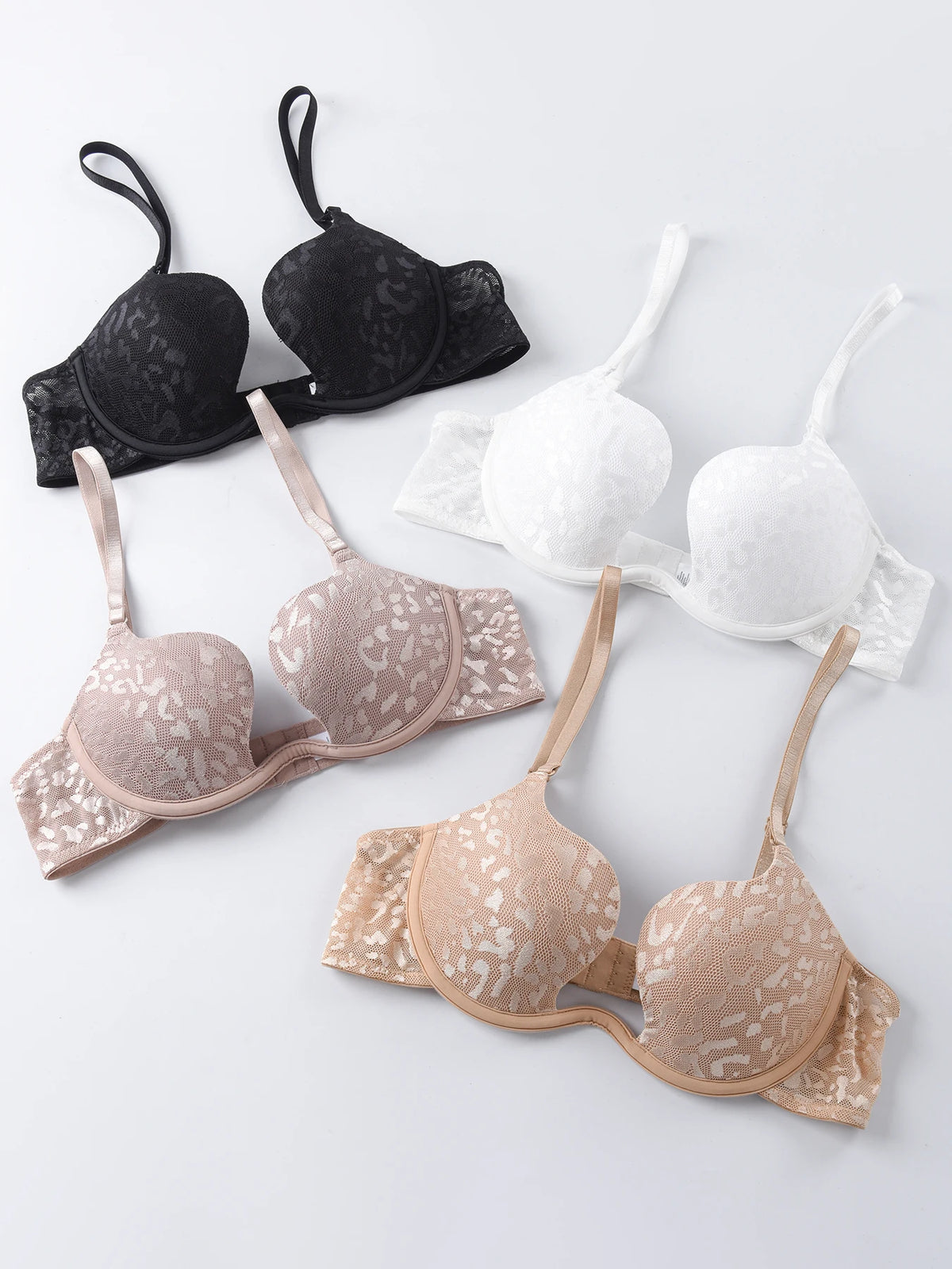 Four lace underwire bras in black, white, and nude shades, arranged diagonally on a light gray background.