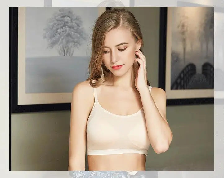 A woman wearing a light beige wireless bralette, posing indoors with framed wall art in the background.