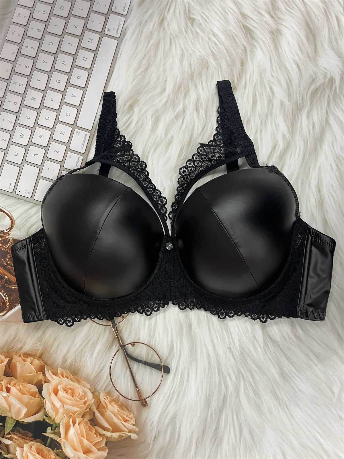 Black bra with lace details on a fluffy white surface with a keyboard and flowers.