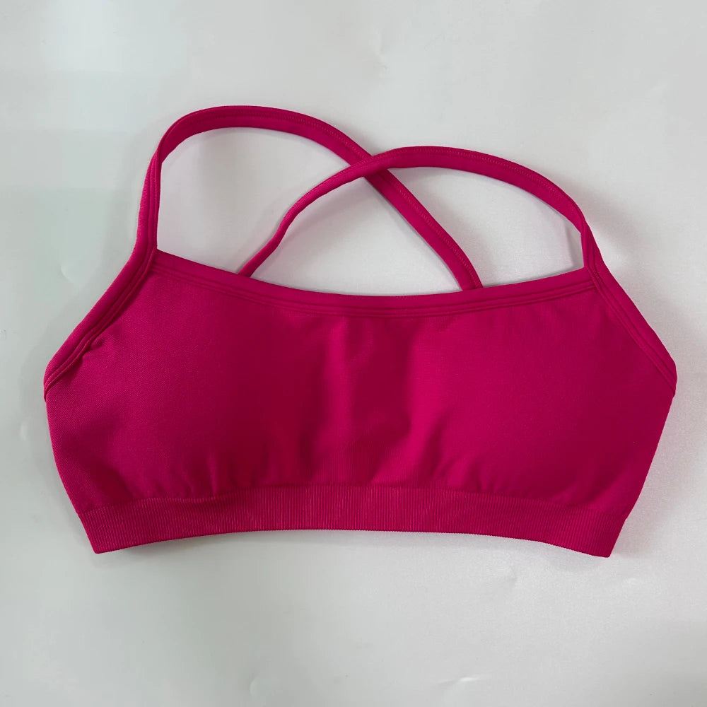 A bright magenta pink sports bra with a square neckline and crisscrossing shoulder straps, laid flat on a light gray background.