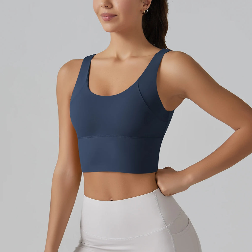 Woman wearing a blue sports bra and white leggings on a gray background