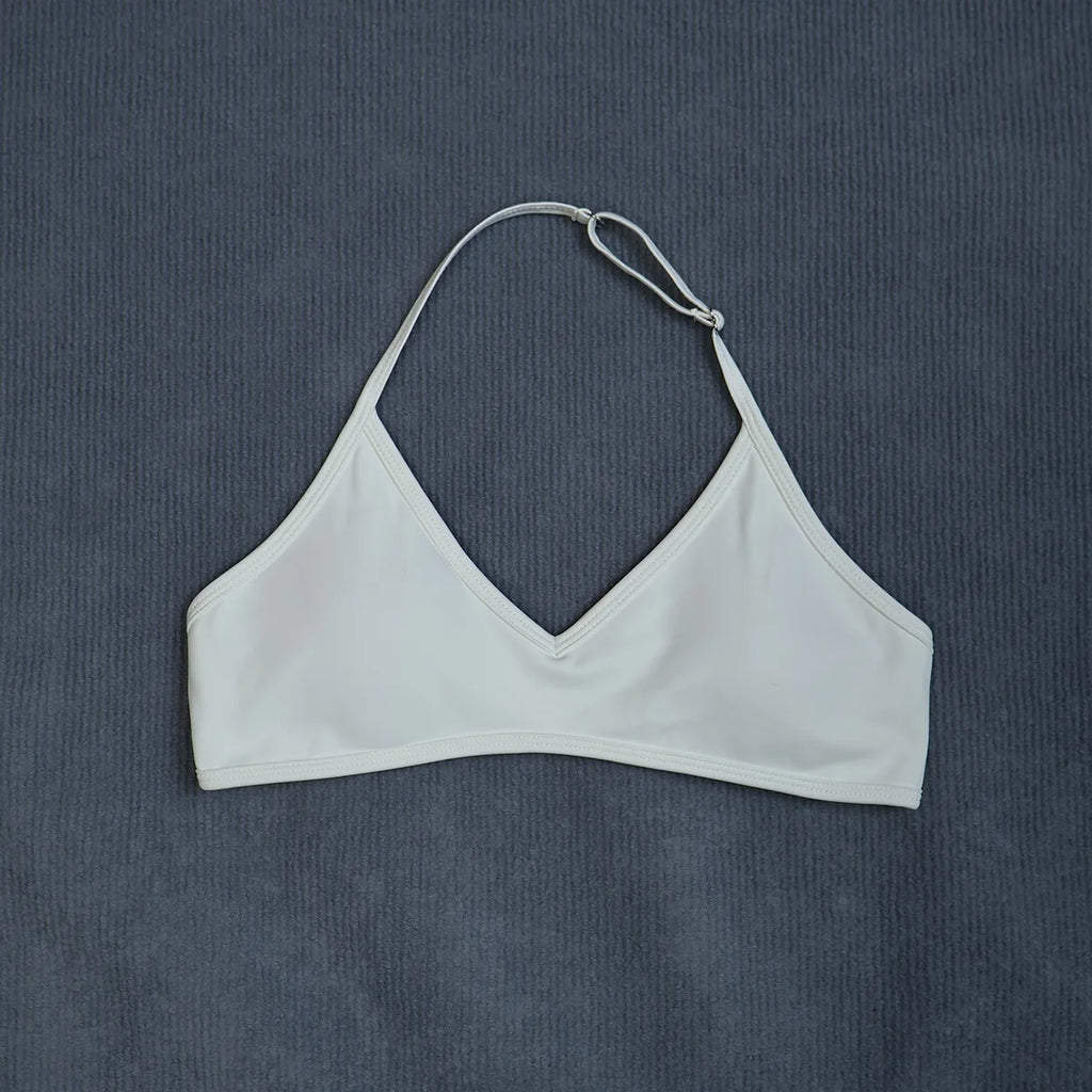 A white halter bikini top with a V-neckline, laid flat on a textured dark gray background.