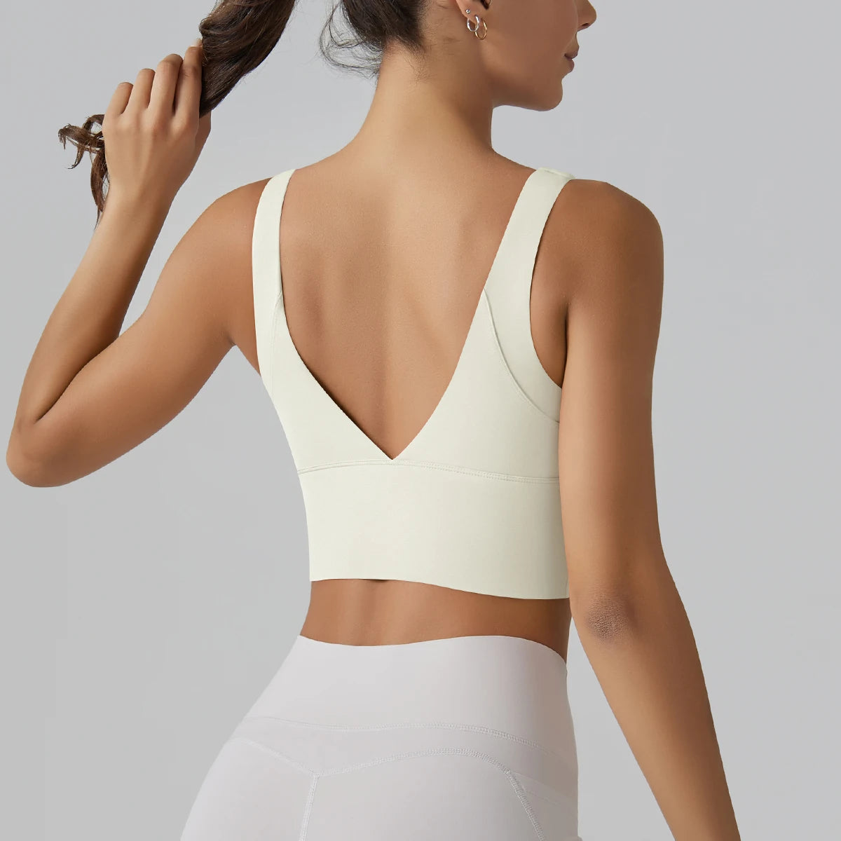 Woman wearing a white sports bra and leggings on a gray background