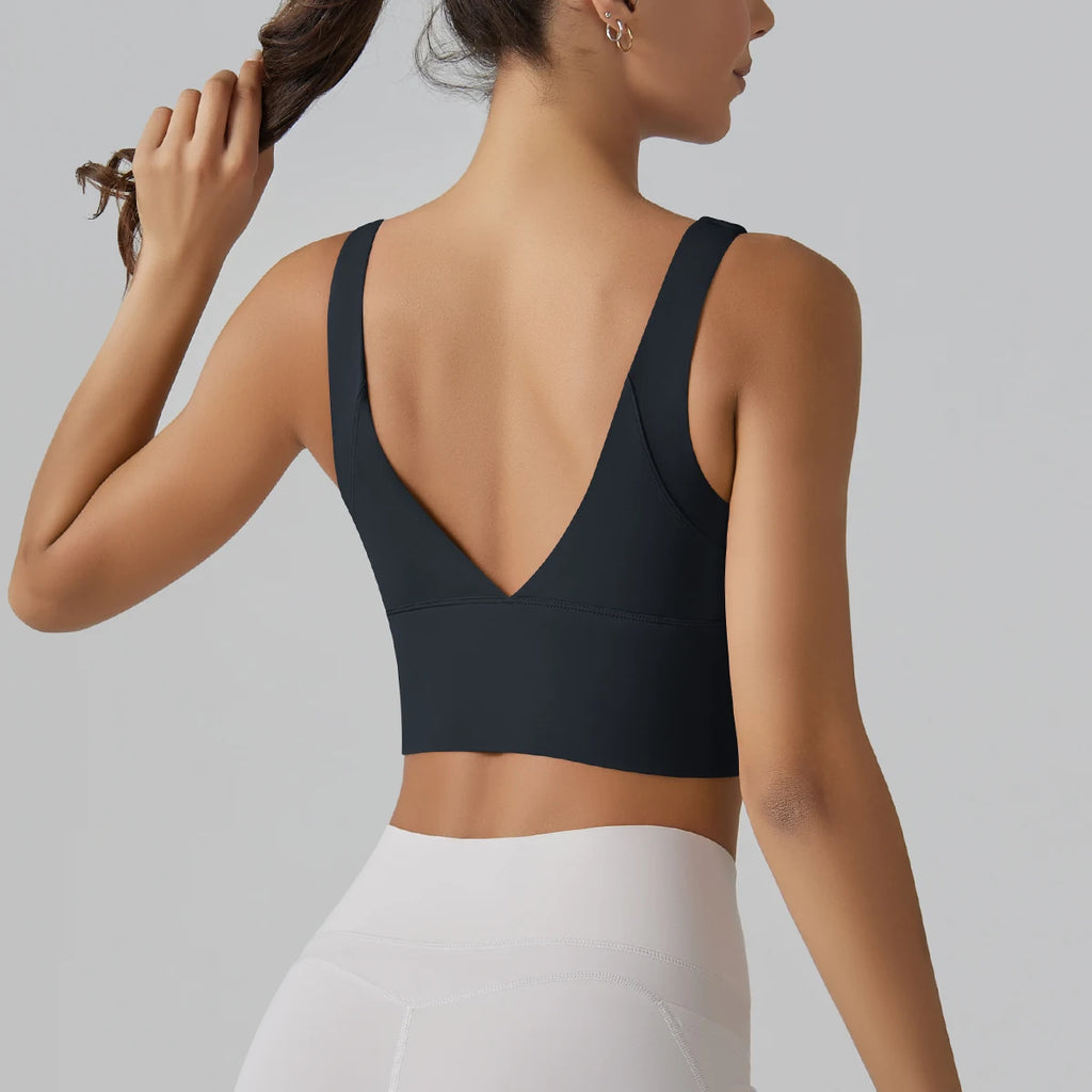 Woman wearing a black sports bra and white leggings on a gray background