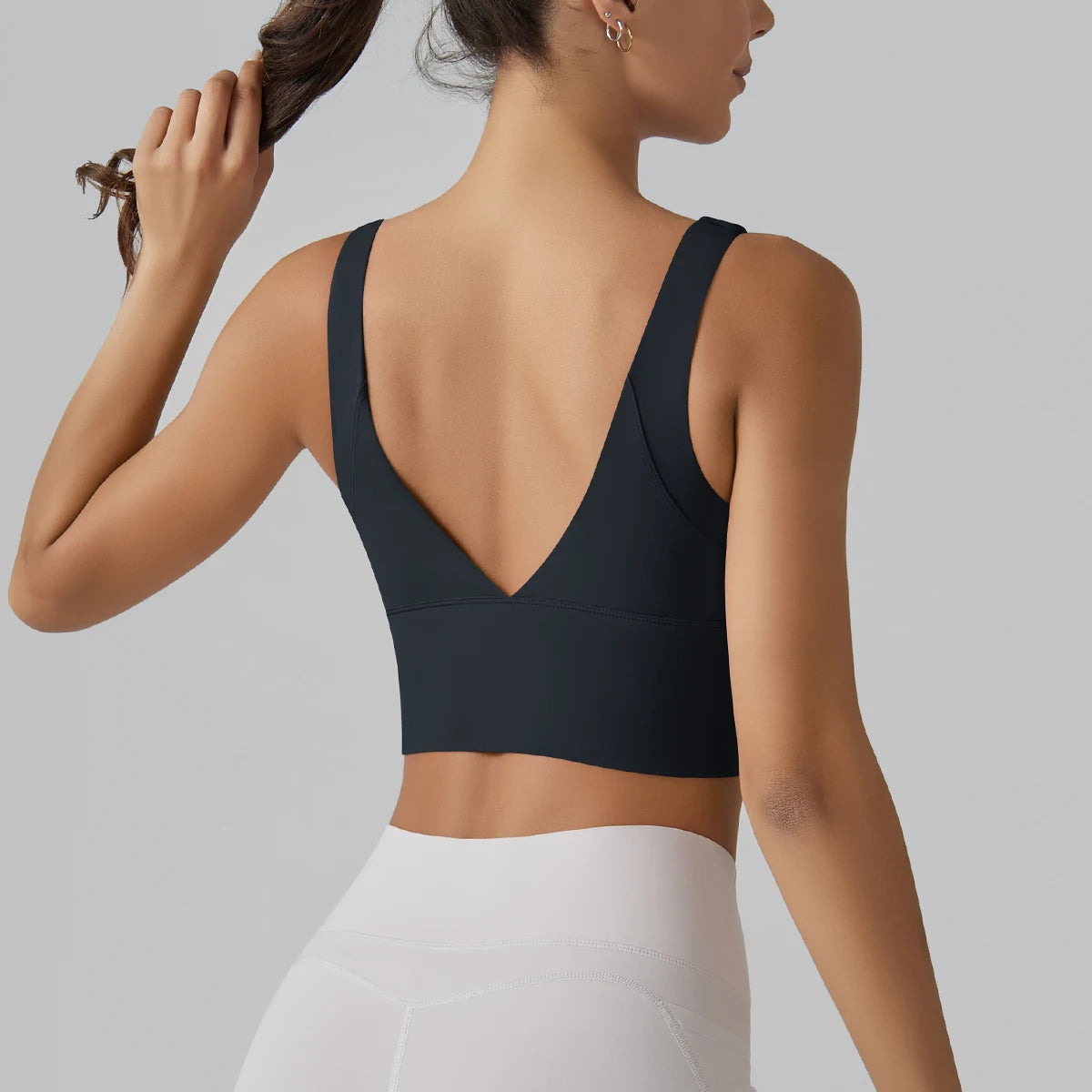Woman wearing a black sports bra and white leggings on a gray background