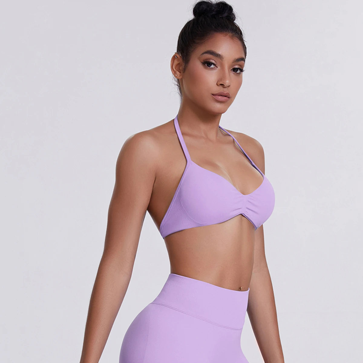 Woman wearing a purple sports bra and leggings on a light gray background