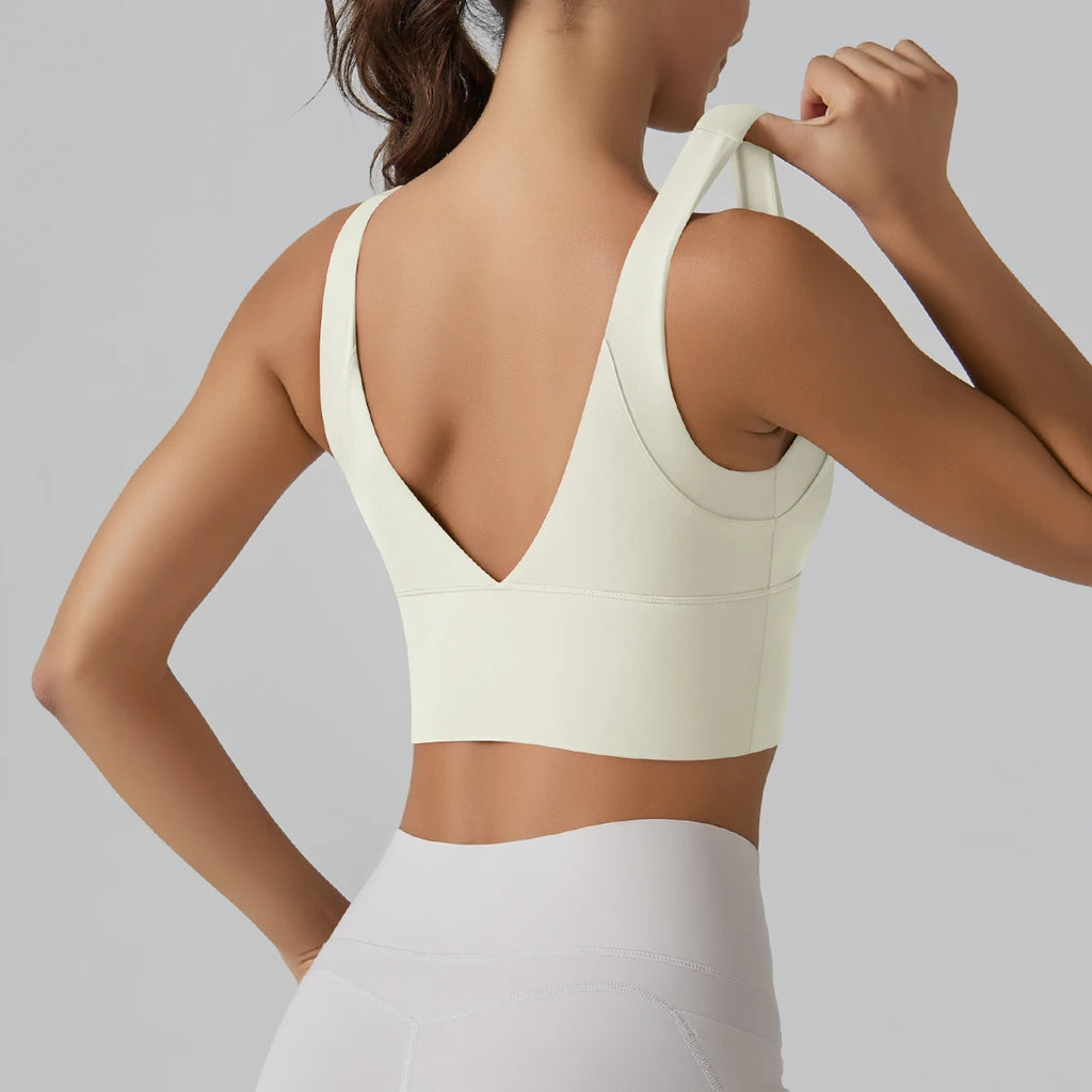 Woman wearing a light-colored sports bra and leggings against a plain background