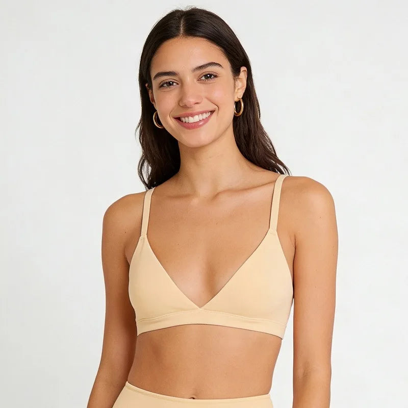A woman wearing a light beige wireless triangle bralette with thin shoulder straps, shown from the chest up against a plain light gray studio background.