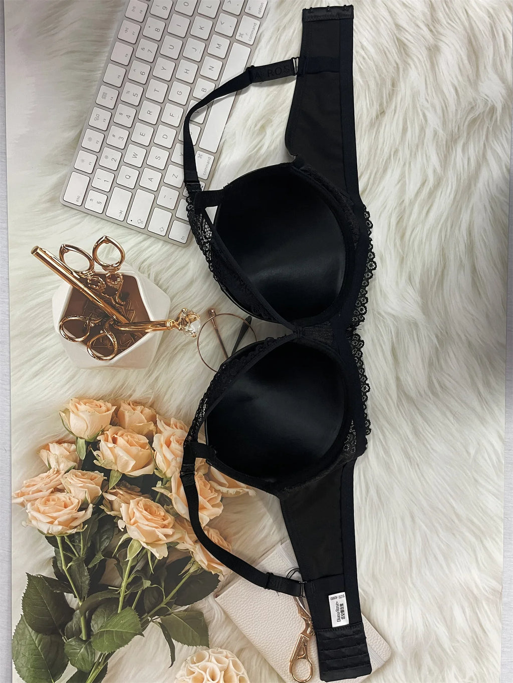Black bra on a white fur surface with flowers and a keyboard in the background