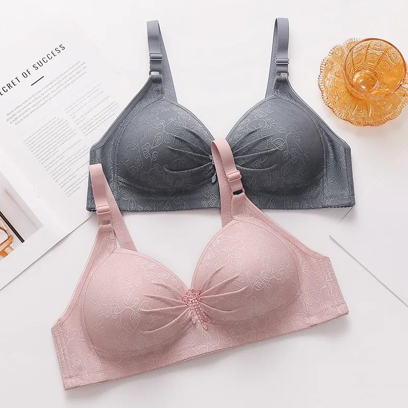 Two bras, one gray and one pink, on a white surface with a magazine and decorative item.