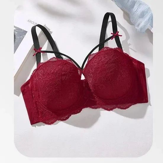A red lace underwire bra with black straps and small red bow accents, displayed on a white surface with soft shadows.