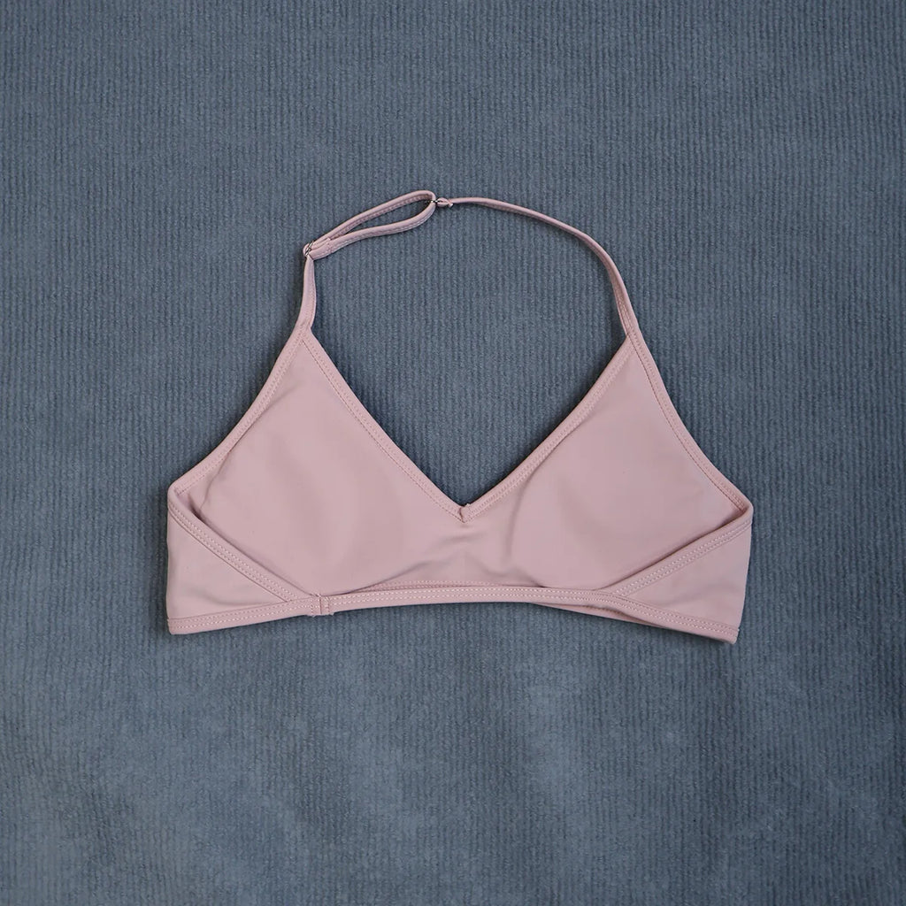 A dusty pink halter bikini top laid flat on a textured slate blue background.