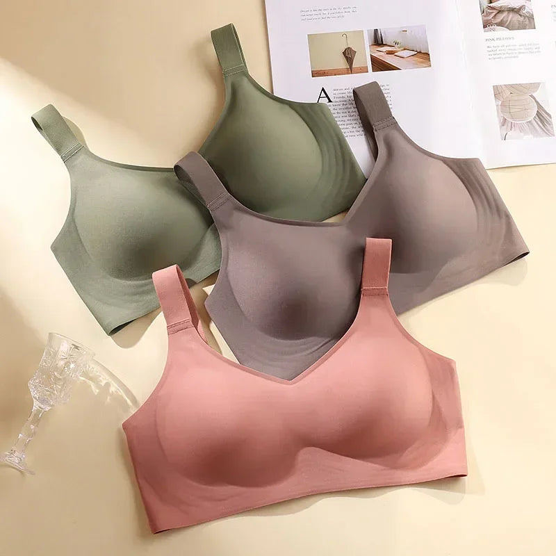 Three bras in green, gray, and pink on a beige surface with a magazine in the background.