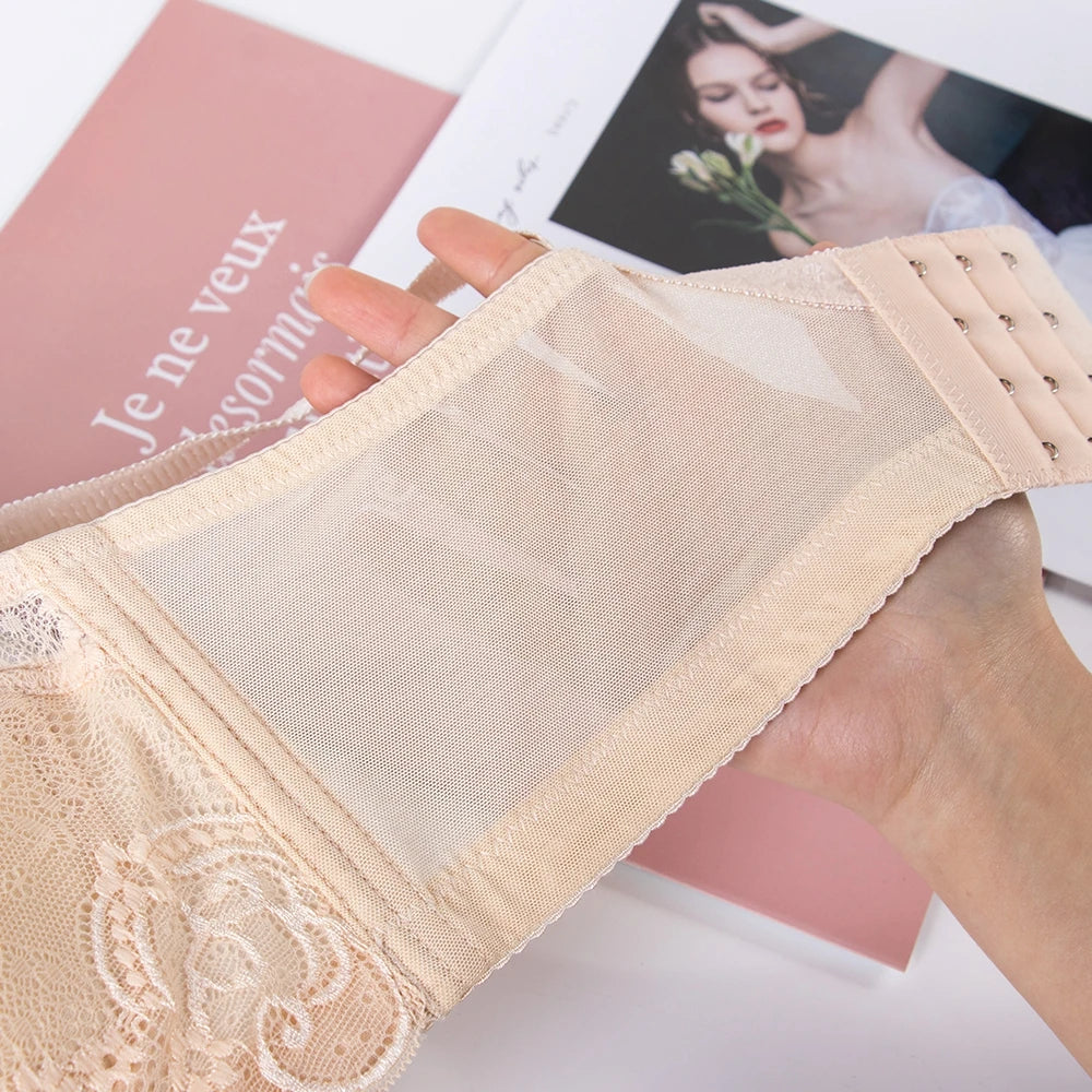 A close-up of a beige lace and mesh bra cup held by a hand, showing the fabric texture and underwire details, with a pink magazine in the background.